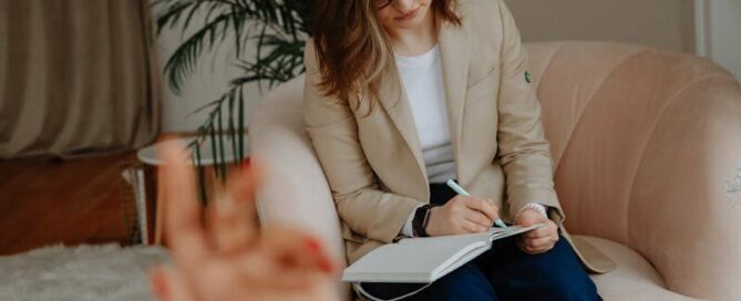 A therapist in a modern office takes notes while listening to a client.